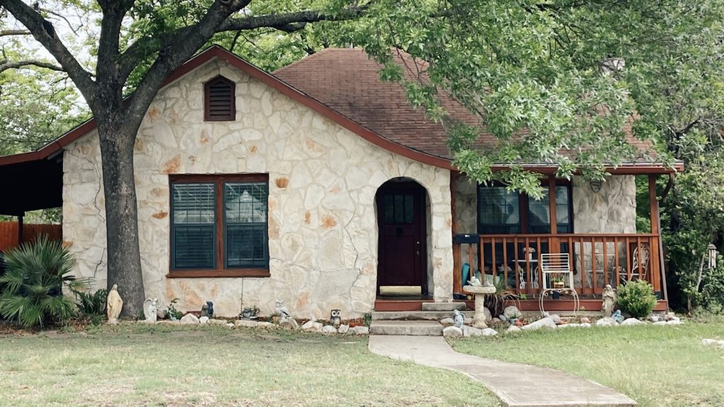 Cottage house with light stone exterior and a Tudor roof line.